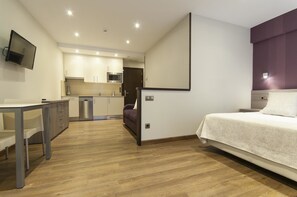 A compact hotel room with a bed, a desk, and a kitchenette. - Apartamentos Turisticos LLanes (Llanes)