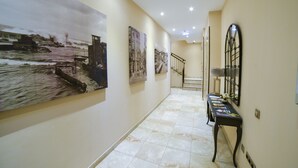 Un couloir orné de grandes peintures représentant des paysages urbains, un escalier et une console sur laquelle sont posés des livres.