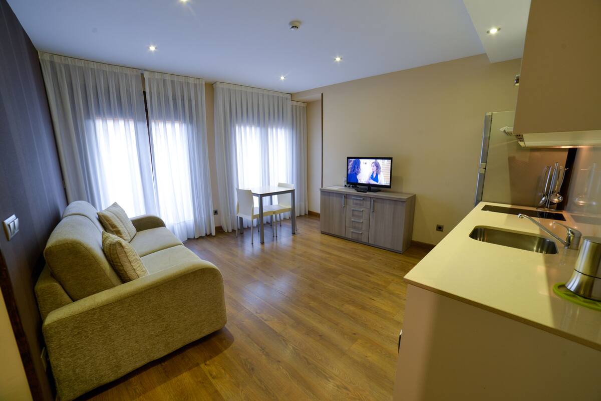 A modern living room with a sofa, a TV, a dining table, and a kitchen area.