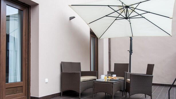 Un balcon agrémenté de meubles en osier, une table avec des aliments pour le petit-déjeuner et un grand parasol.