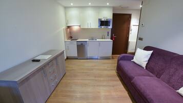 Un espacio habitable compacto con kitchenette, un sofá púrpura y piso de madera.