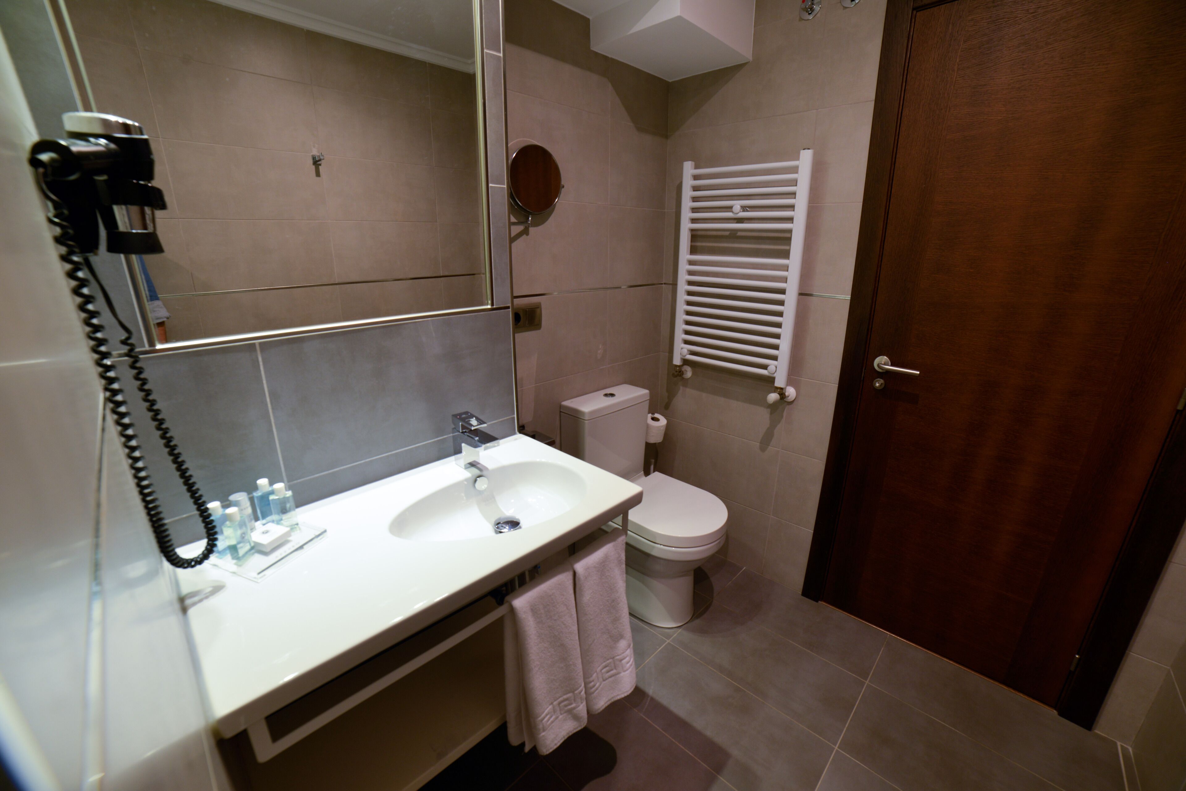 Een badkamer met een wit wastafelmeubel, toilet en een houten deur.