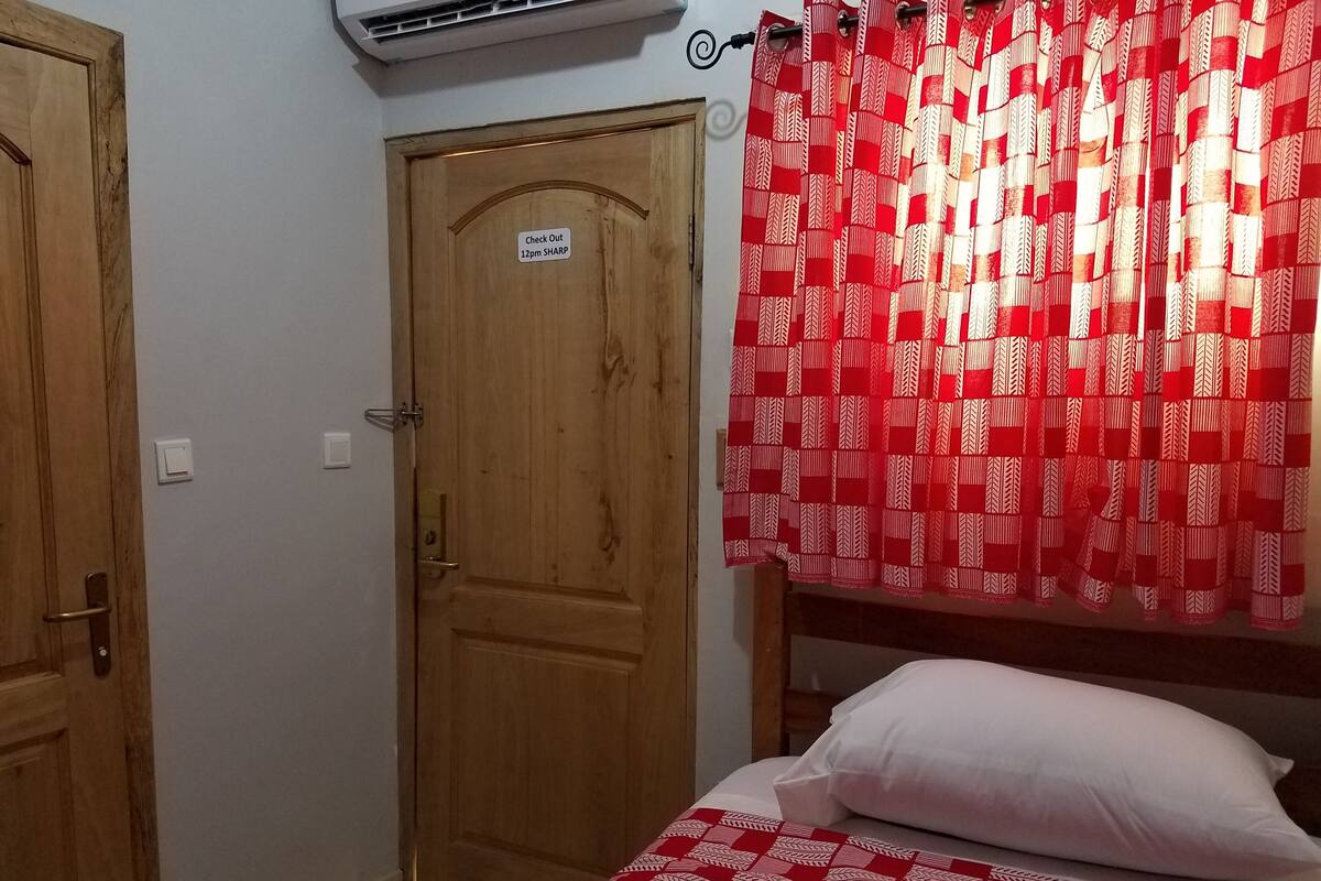 Una habitación con puerta de madera, una cama con colcha de rayas rojas y blancas y una almohada blanca.