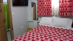 A bedroom with a bed, a TV mounted on the wall, and red patterned curtains. - Sharp Guest House (Accra)