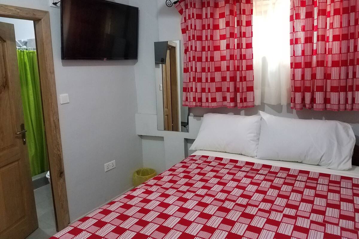 Un dormitorio con una cama, un televisor montado en la pared y cortinas rojas con estampado.