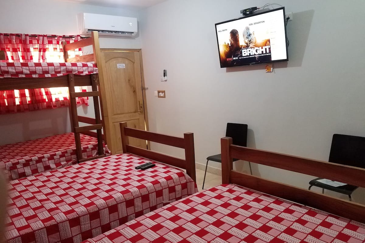 Una habitación con tres literas, cada una con un edredón a cuadros rojo y blanco. Hay un televisor montado en la pared que muestra un cartel de cine.