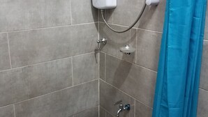 A shower area with grey tiles, a handheld showerhead, a wall-mounted control panel, and a blue shower curtain. - Sharp Guest House (Accra)