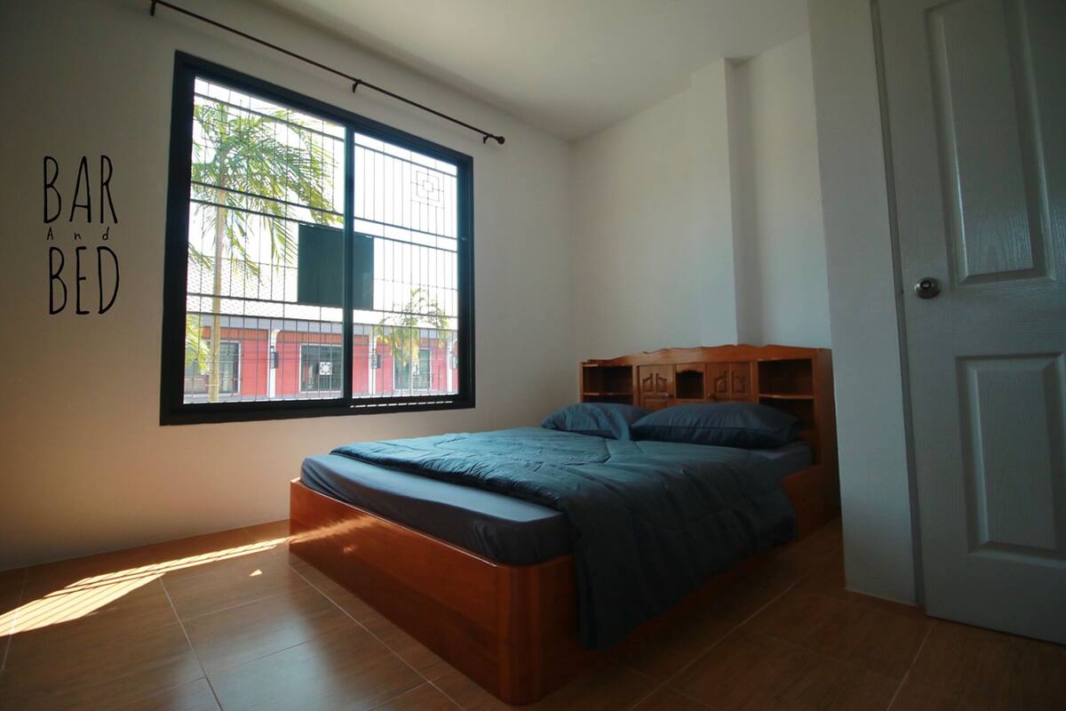 A bedroom with a large window, a bed, a wardrobe, and a door.