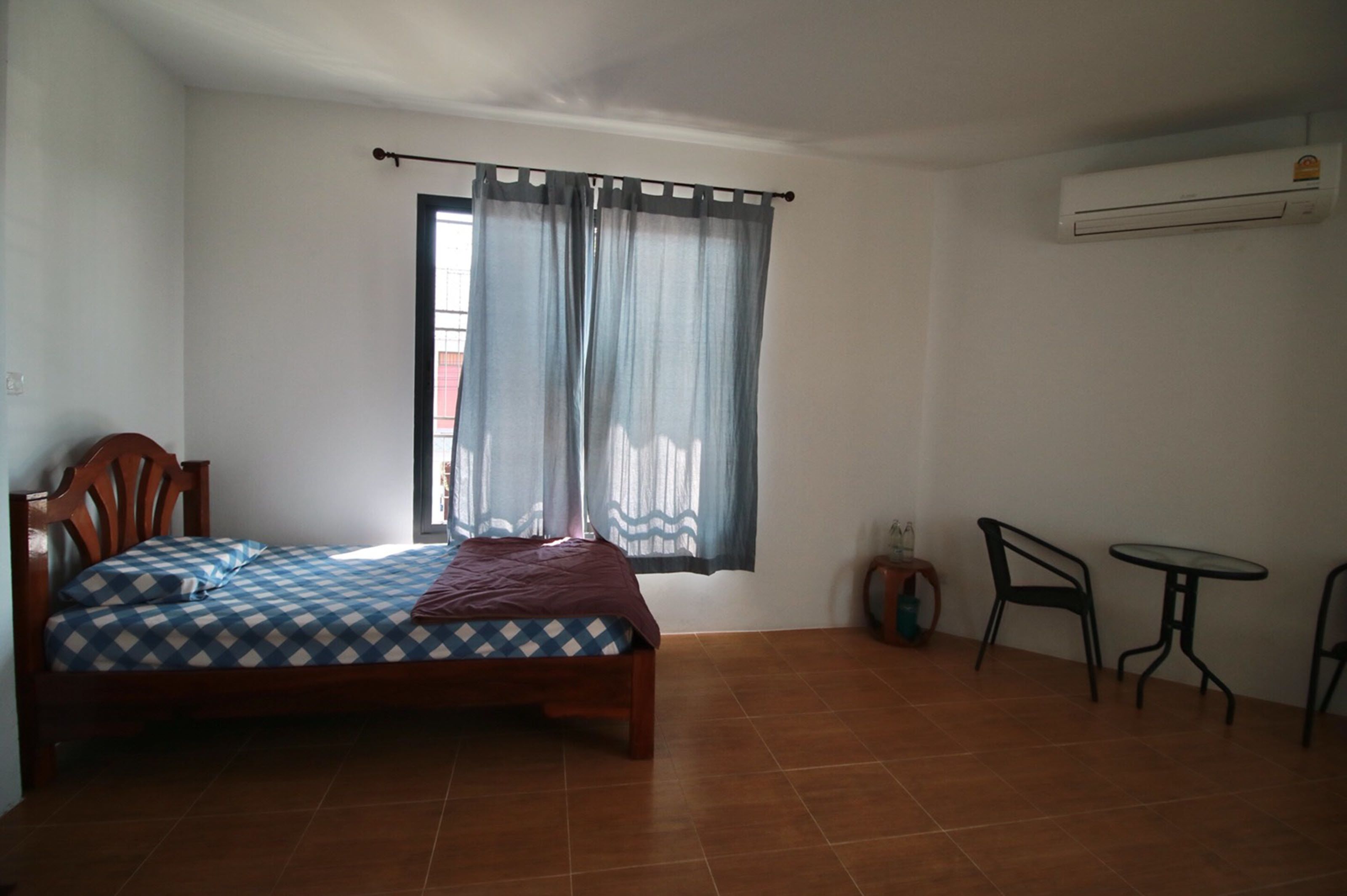 A bedroom with a bed, a window with curtains, a small table, and a chair.