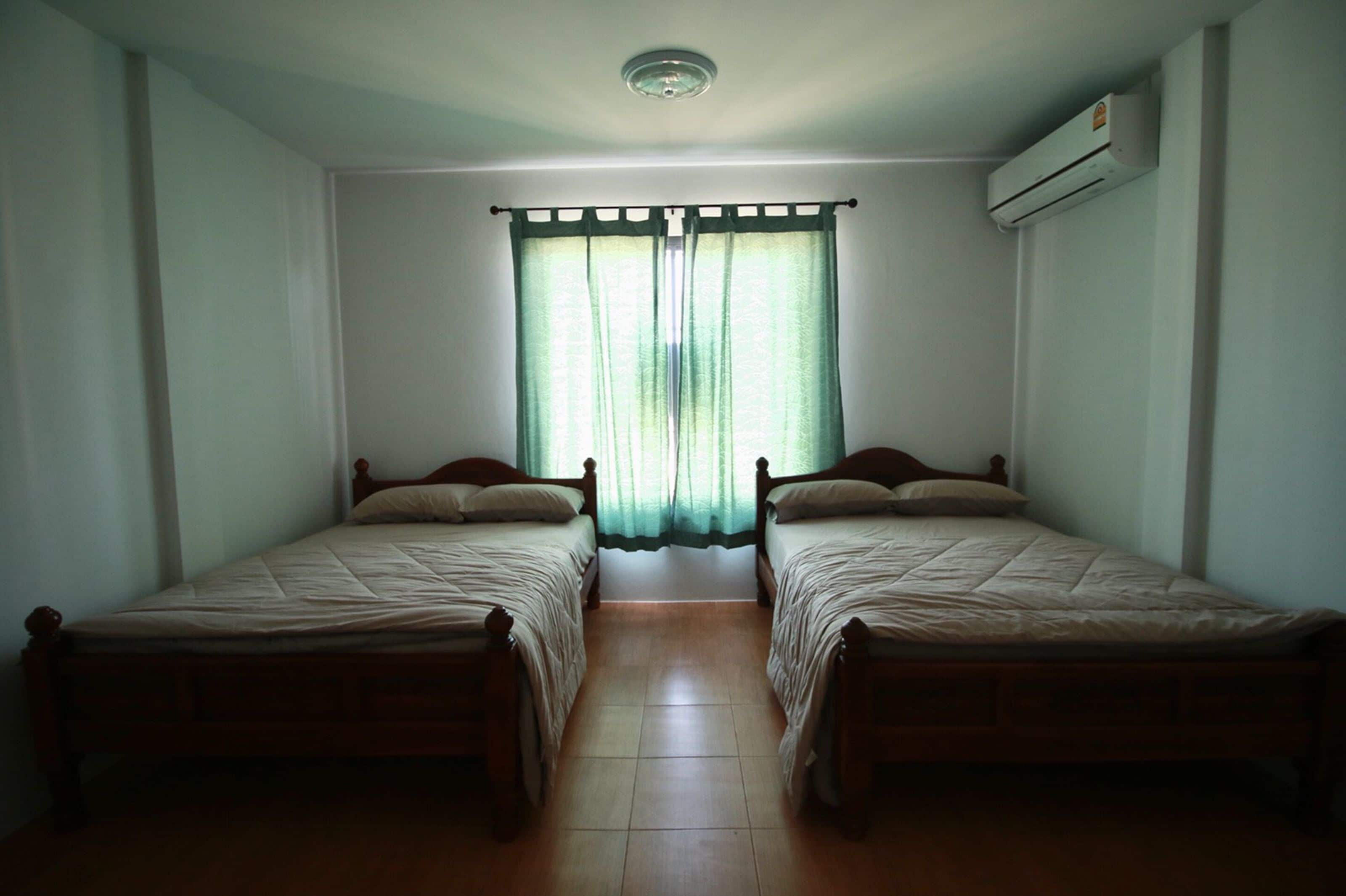 Une chambre avec deux lits simples, une fenêtre avec des rideaux, un appareil de climatisation et un sol carrelé.