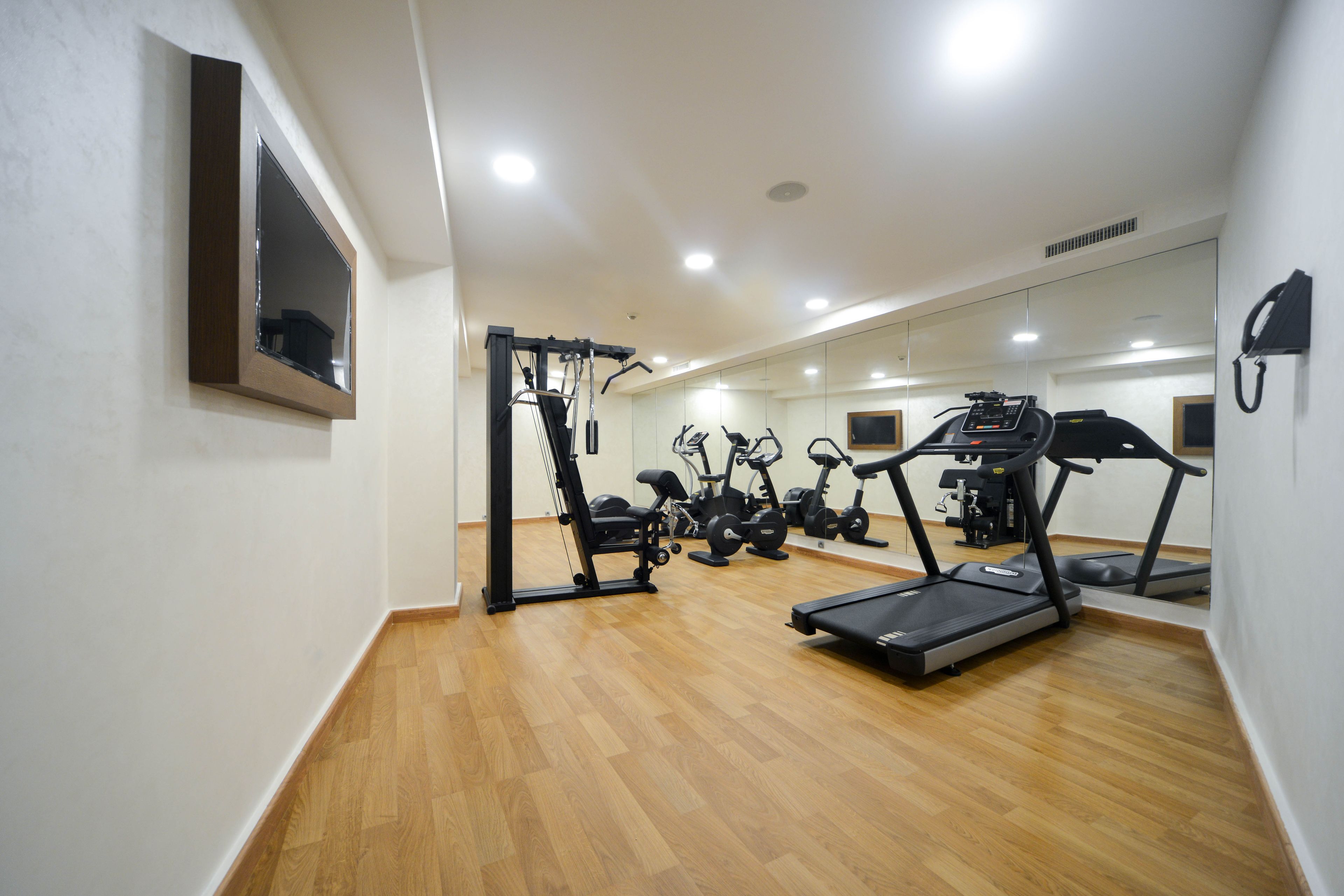 A gym with exercise equipment, wooden flooring, and mirrors on the walls.