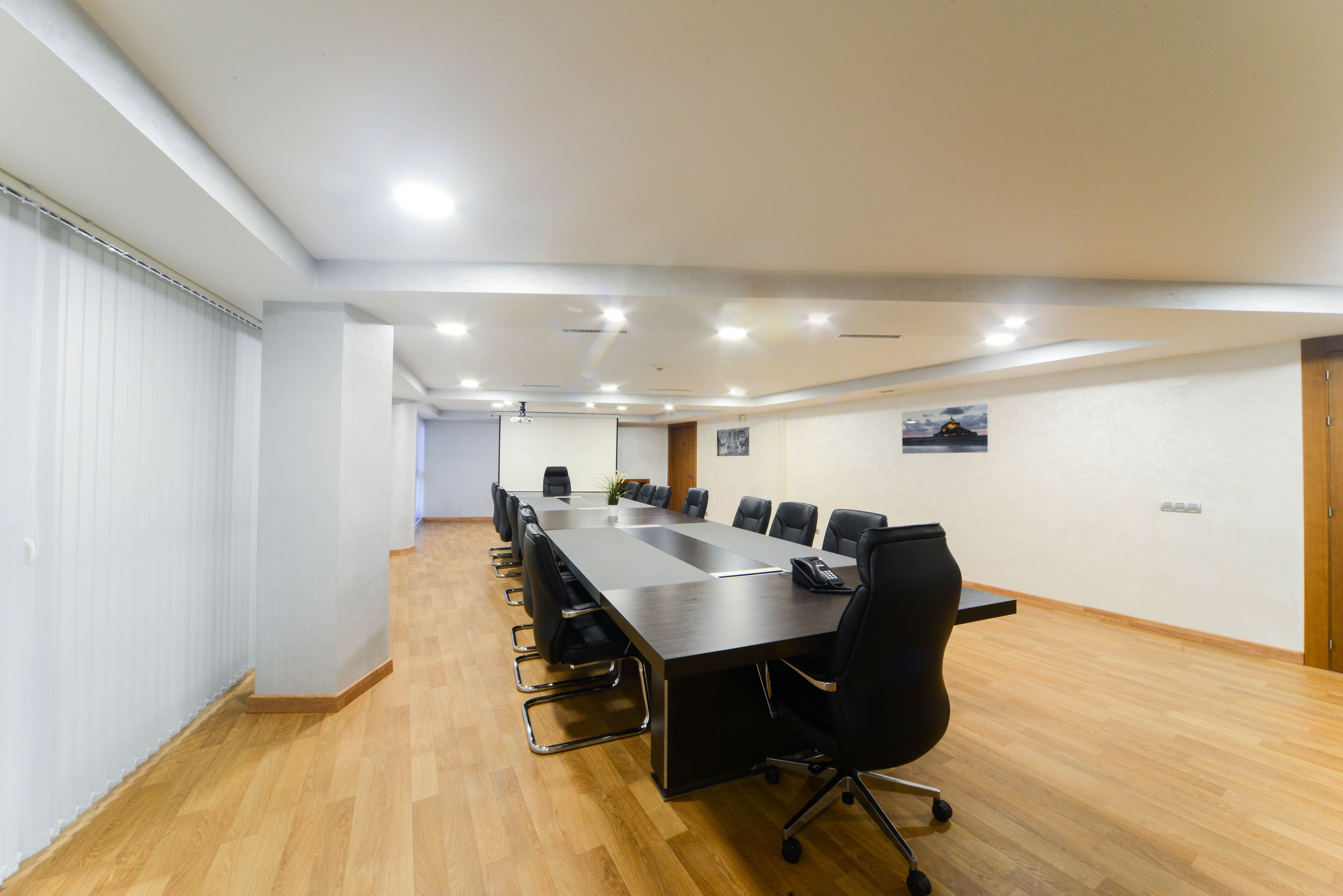 Une salle de conférence avec une longue table, des chaises noires et un éclairage encastré au plafond.
