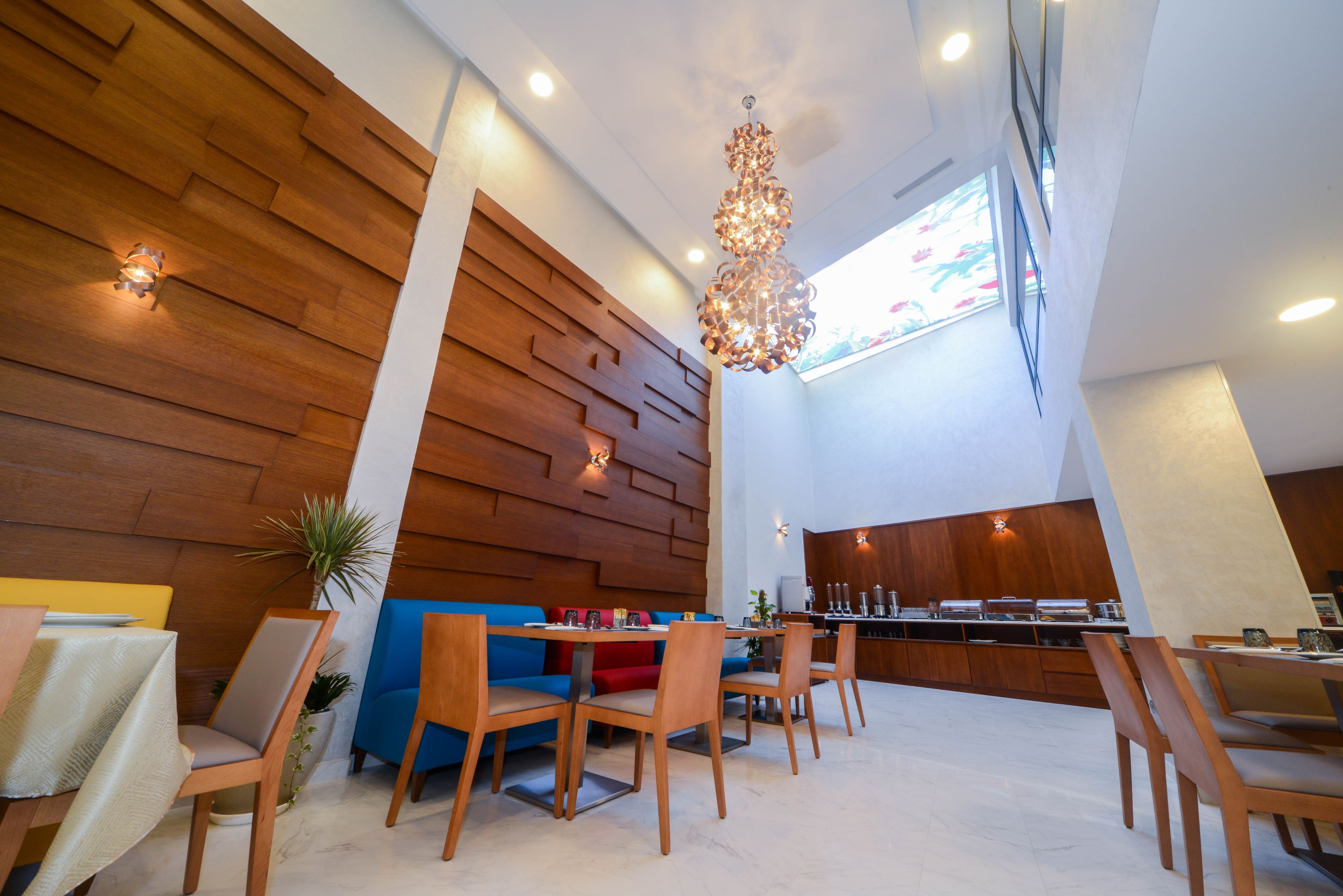 Un espace de salle à manger moderne avec des murs lambrissés en bois, un lustre central et un aménagement comprenant un canapé et des fauteuils.
