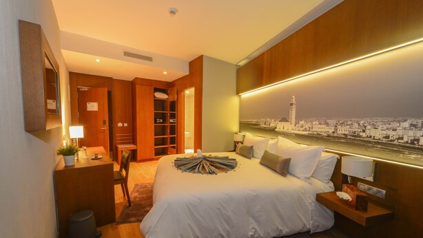 Een moderne hotelkamer met een groot bed, nachtkastjes, een bureau en uitzicht op een stadsbeeld.
