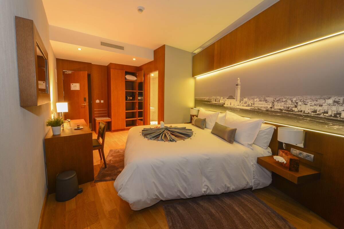 Een moderne hotelkamer met een groot bed, nachtkastjes, een bureau en uitzicht op een stadsbeeld.