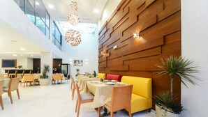 Een moderne eetruimte met gele banken, houten stoelen en gedekte tafels.