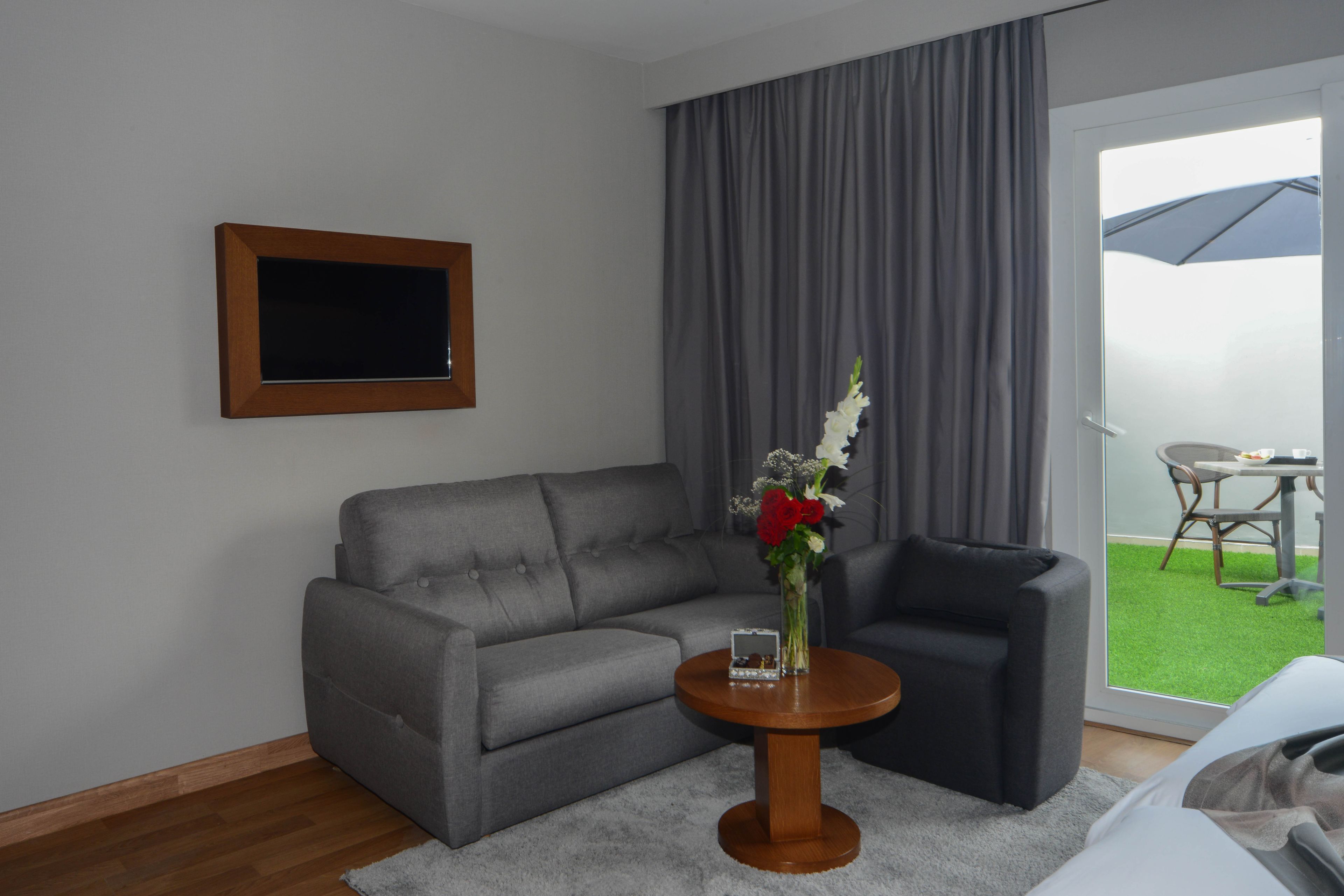 Un salon moderne avec un canapé gris, un fauteuil noir et une table basse ronde en bois sur laquelle est posé un vase de fleurs.