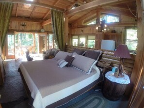 A wooden cabin bedroom with a large bed, a small table, and a window. - Lanzarotta Bed and Breakfast (Eugene)