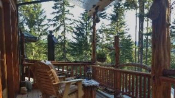 A wooden deck with a chair and a small table, surrounded by a wooden railing and trees in the background. - Lanzarotta Bed and Breakfast (Eugene)