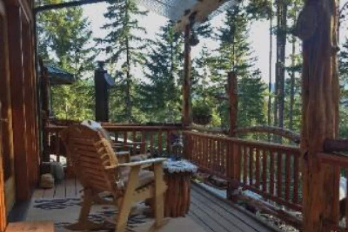 A wooden deck with a chair and a small table, surrounded by a wooden railing and trees in the background.