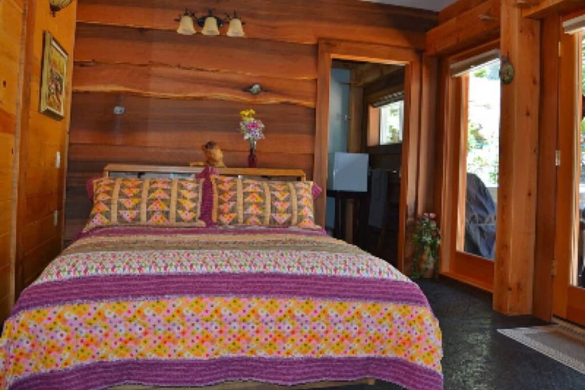 A wooden cabin bedroom with a bed, a wooden headboard, and a door leading to a porch.