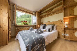 Une chambre à coucher en bois, avec un lit, une fenêtre donnant sur un paysage verdoyant, une commode et une table de chevet avec une lampe.