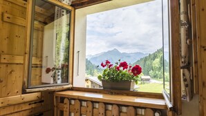 Une cabane en bois dotée d’une grande fenêtre, d’un banc en bois et d’une plante en pot ornée de fleurs rouges.