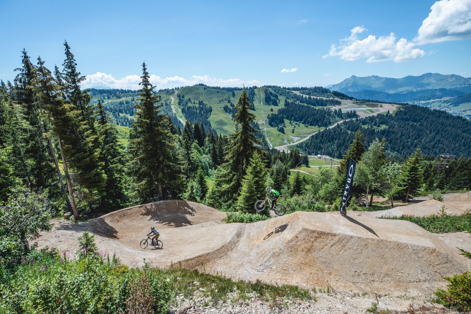 A mountain biking trail with a dirt path, surrounded by dense forests and distant mountain ranges.
