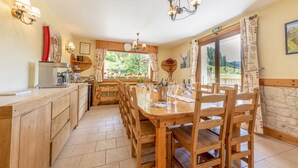 Un coin repas en bois avec vue sur l’extérieur, un comptoir en bois équipé d’appareils de cuisine et un lustre.