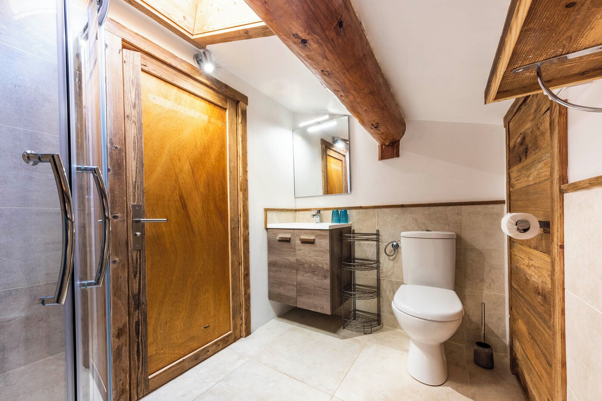 A bathroom with a wooden door, a white toilet, a sink with a mirror above it, and a shower area.
