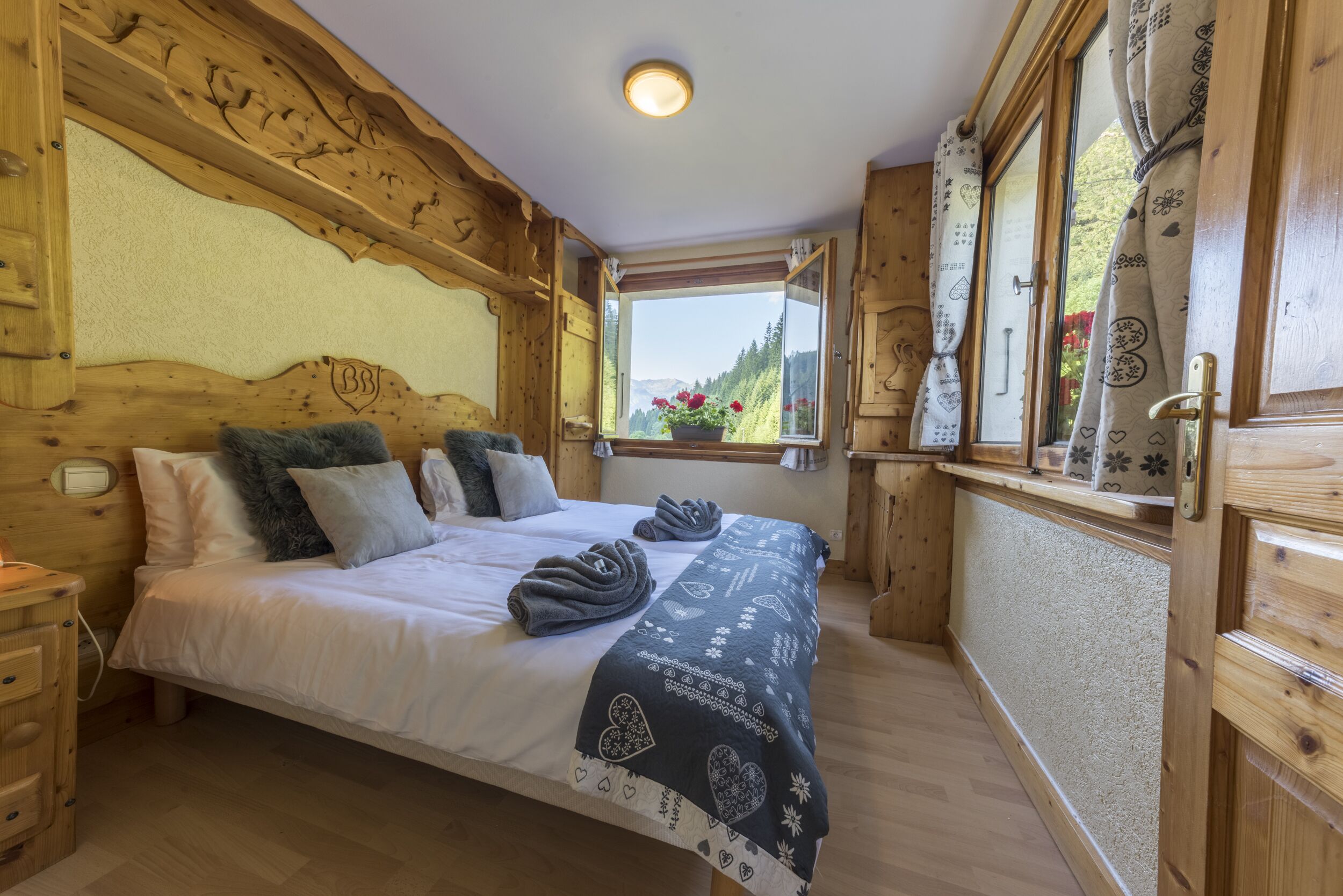 A wooden cabin bedroom with a bed, pillows, a window with curtains, and a wooden headboard.