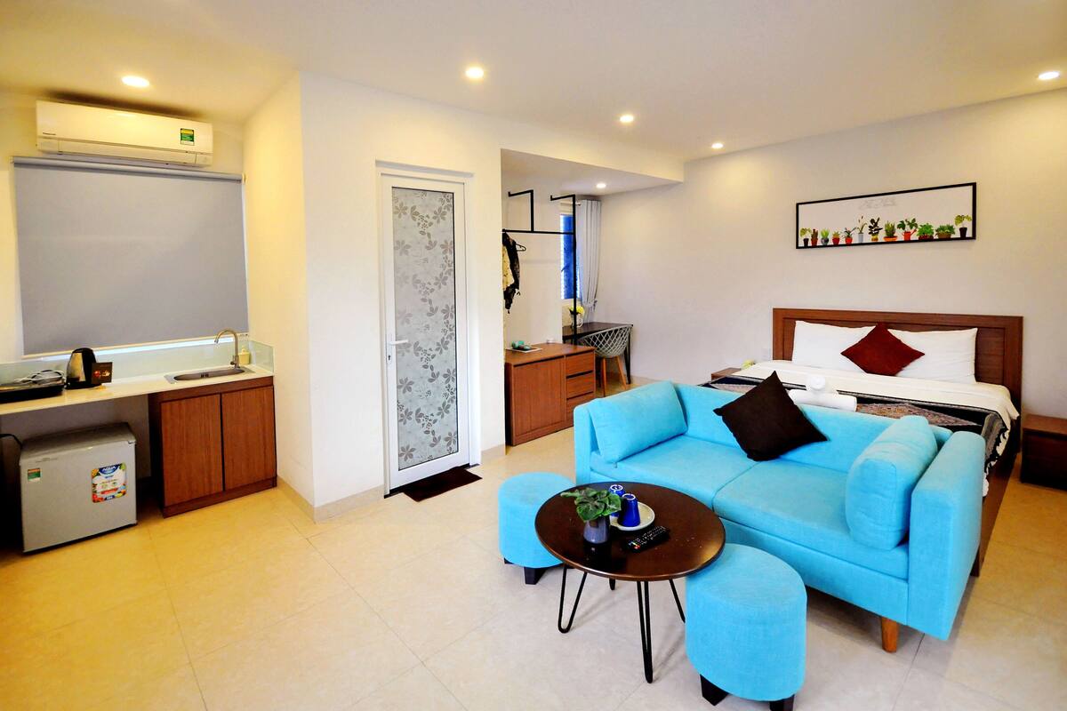A compact hotel room with a kitchenette, a sofa, a small table, and a bed.