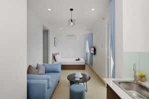 A modern hotel room with a bed, a sofa, a small round table, and a kitchenette area.