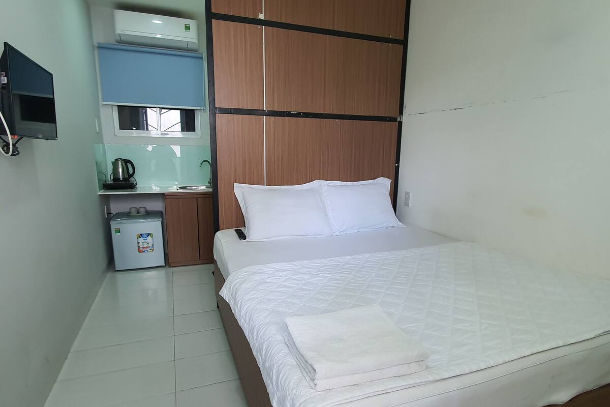A hotel room with a bed, a small kitchenette, a sink, and a television.