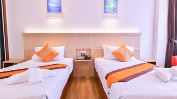 A hotel room with two beds, each with white bedding and orange accents, a wooden headboard, and a bedside table with a phone.