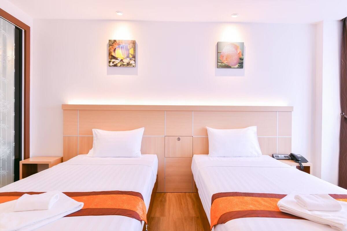 A hotel room with two beds, a wooden headboard, a nightstand with a phone, and two wall-mounted artworks.