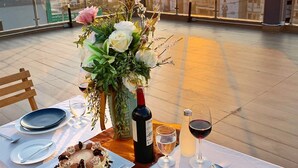 A table set for two with a dessert, wine, and a floral centerpiece on a rooftop terrace during sunset. - Marlin Hotel (Surat Thani)