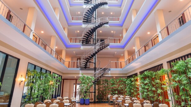 A spacious hotel lobby with a central spiral staircase, multiple seating areas, and indoor plants. - Marlin Hotel (Surat Thani)