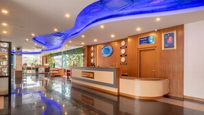 A hotel reception area with a modern design, featuring a reception desk, clocks displaying multiple time zones, and a blue-lit ceiling. - Marlin Hotel (Surat Thani)