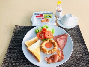 A breakfast plate with toast, eggs, bacon, tomatoes, and lettuce on a table with a teapot and sugar packets. - Marlin Hotel (Surat Thani)
