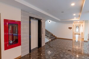 A modern interior with a polished marble floor, a red fire alarm, and a staircase leading to another level.