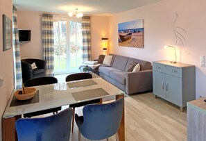 A living room with a sofa, dining table, chairs, a TV, and a lamp.