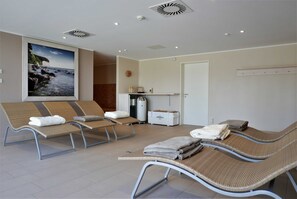 Una habitación con sillones reclinables, un cuadro de una escena costera, una pequeña cocina americana y una puerta.