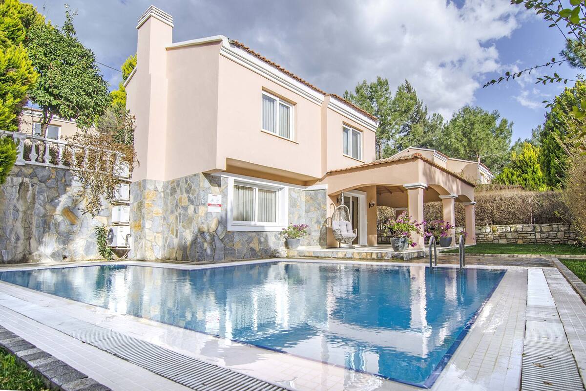A two-story house with a swimming pool, stone walls, and a covered patio area.