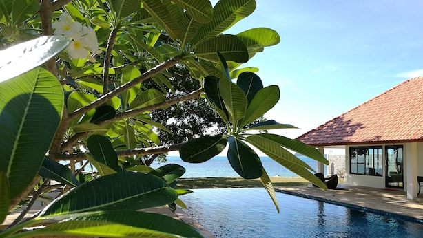 A poolside area with a view of the sea, surrounded by lush greenery and a building with a tiled roof. - Heaven Beach Resort (Koh Samui)