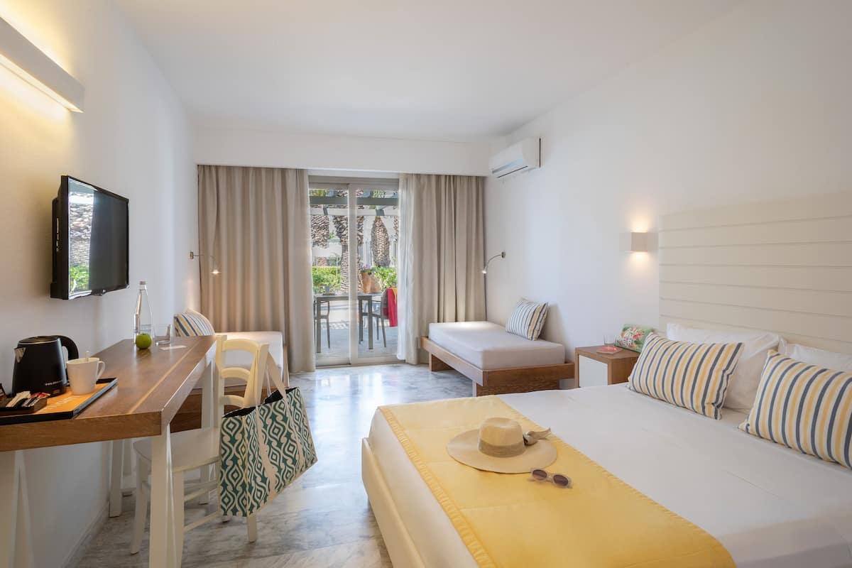 A hotel room with a bed, a desk, a chair, a TV, and a balcony with curtains.