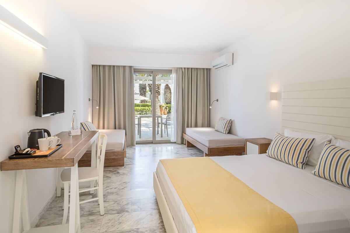 A hotel room with a bed, a desk with a chair, a television, and a balcony with curtains.