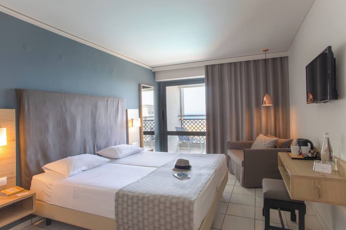 A hotel room with a bed, a desk, a chair, a TV, and a balcony with a view.