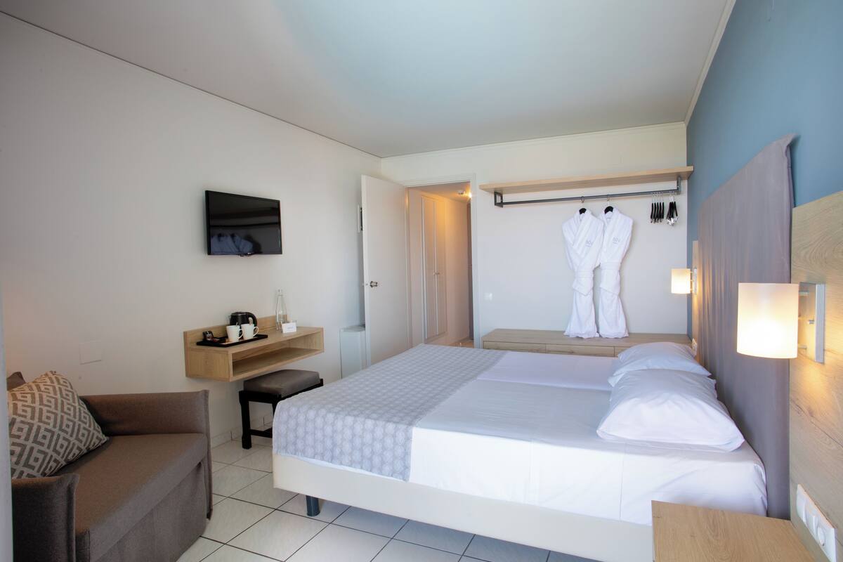 A hotel room with a bed, a desk, a chair, a TV, and a wardrobe.