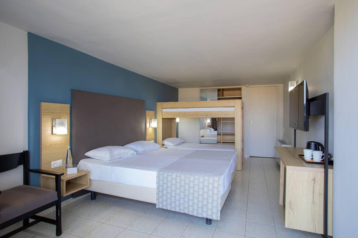 A hotel room with a large bed, a desk, a chair, a TV, and a wardrobe.